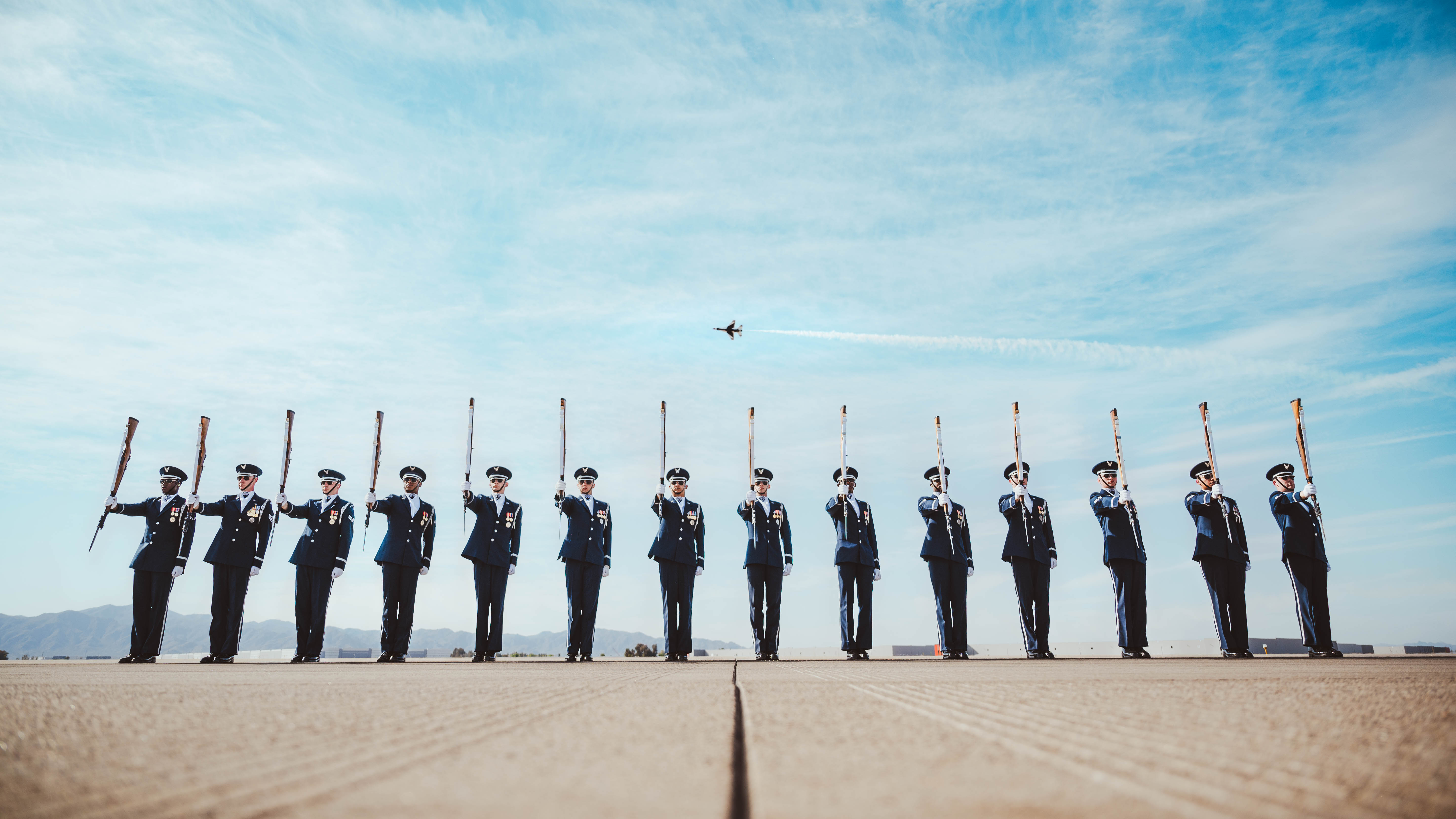 honor guard group in formation as an aircraft fly right behind them