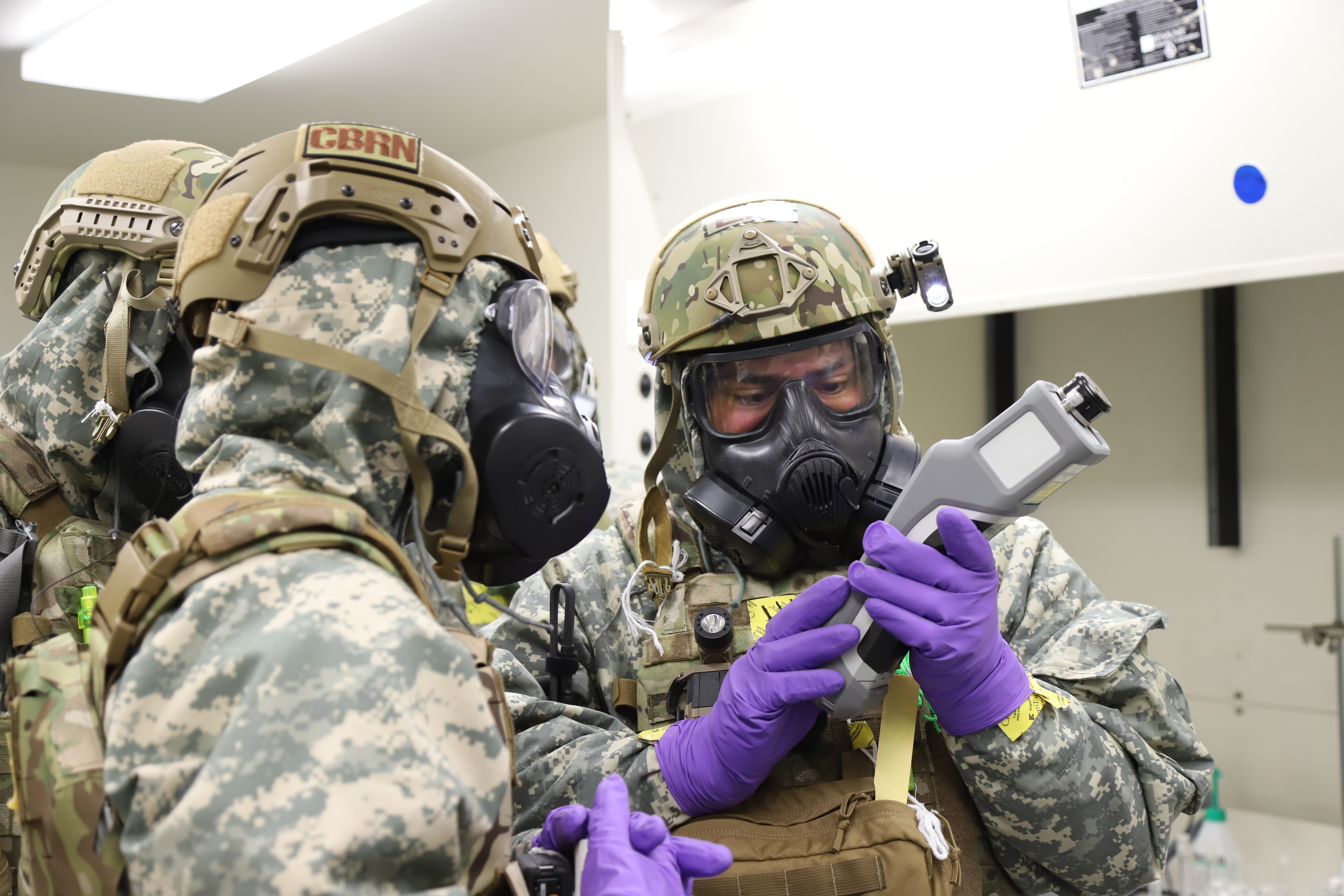 Airmen in protective gear inspecting object