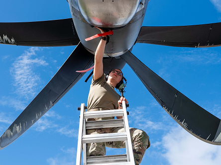 Airman on ladder inspecting bottom of plane.