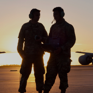 silhouette of two airmen talking to each other with the sun rising in the background